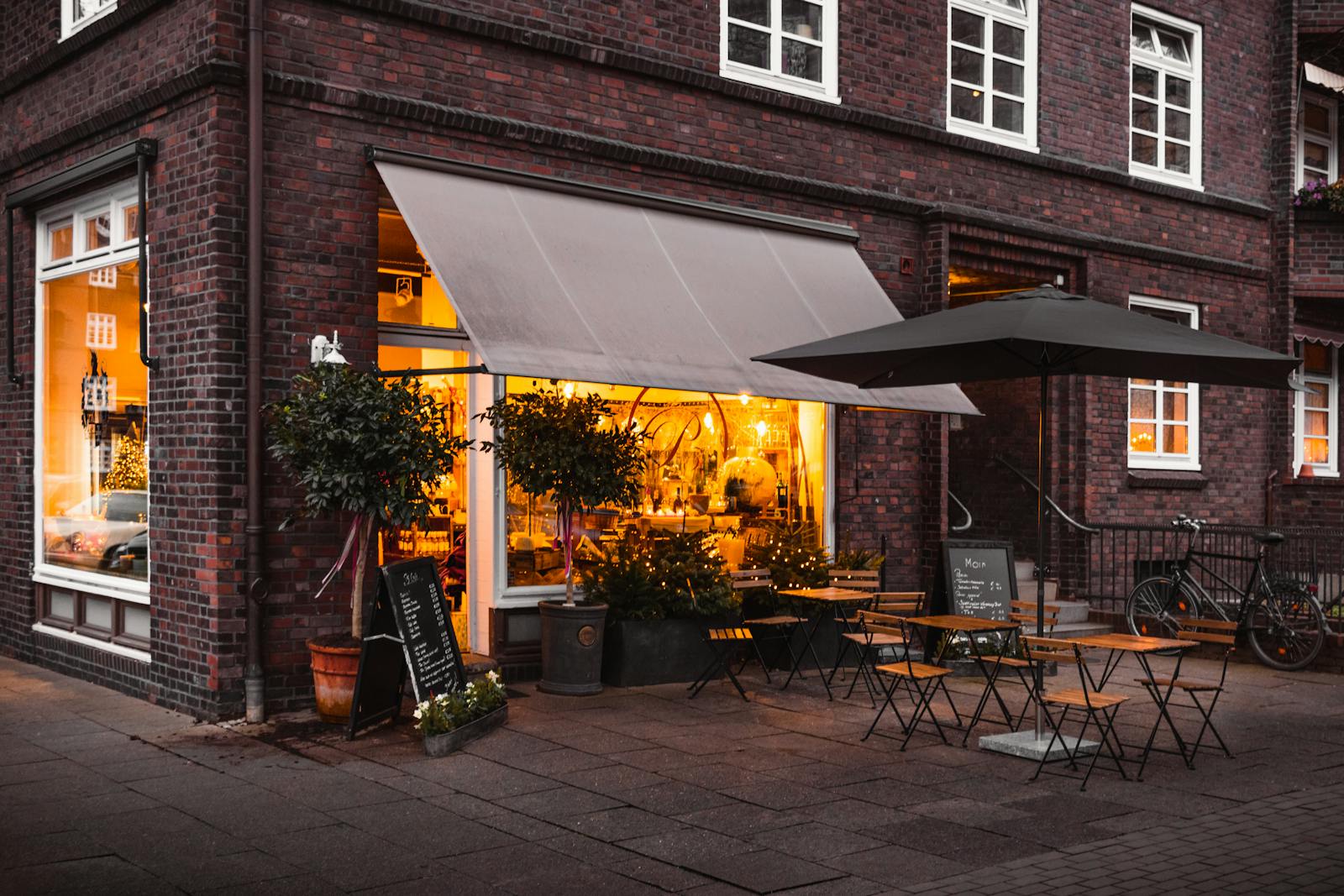 Außenansicht eines charmanten Hamburger Cafés bei Abendlicht mit Markise, Außentischen und Tafelmenü.